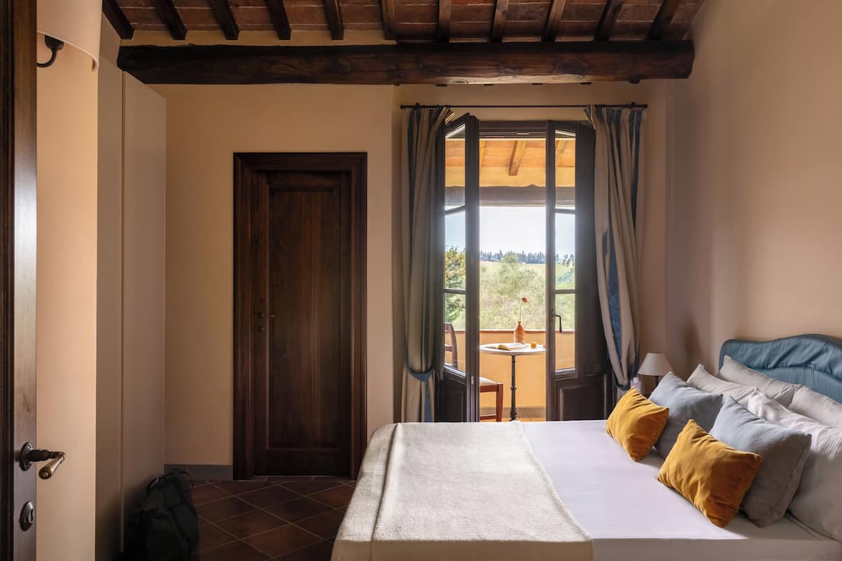 A bedroom with a bed, a window with curtains, a view of the outdoors, and a door.