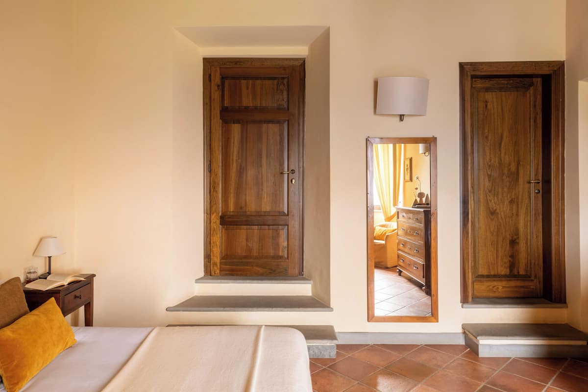 A bedroom with a bed, a nightstand, a lamp, and a wooden wardrobe with a mirror.