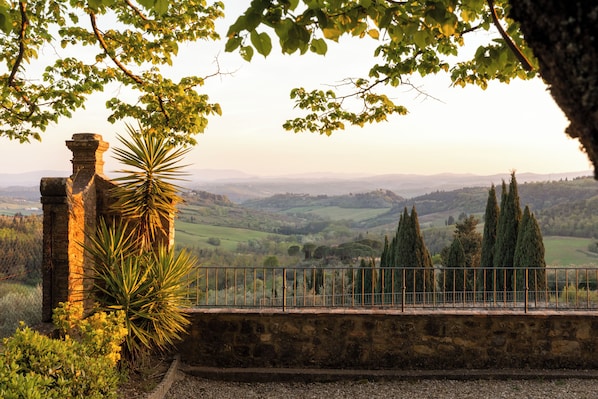 A stone wall with a metal railing, overlooking a valley with trees and distant hills.