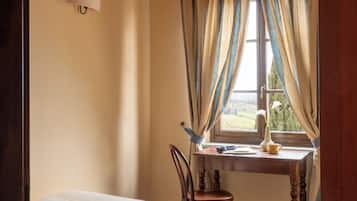 Ein Schlafzimmer mit Bett, Schreibtisch mit Stuhl, einem Fenster mit Vorhängen und einer Wandlampe.