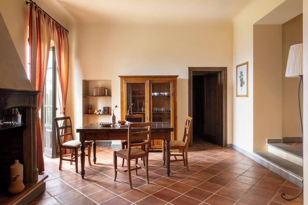 A dining area with a wooden table and chairs, a cabinet with glass doors, a fireplace, and a lamp.
