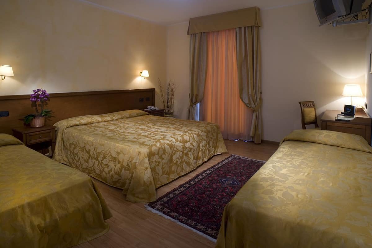 A hotel room with two beds, a TV, a desk with a lamp, and a window with curtains.