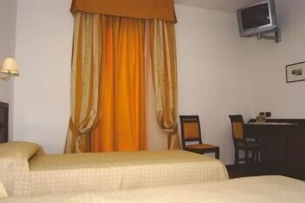 A hotel room with two beds, a television mounted on the wall, a chair, and a small table with items on it.