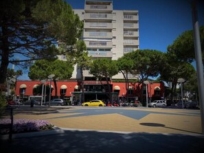 Un hotel de fachada roja, varios pisos y un coche amarillo estacionado adelante.