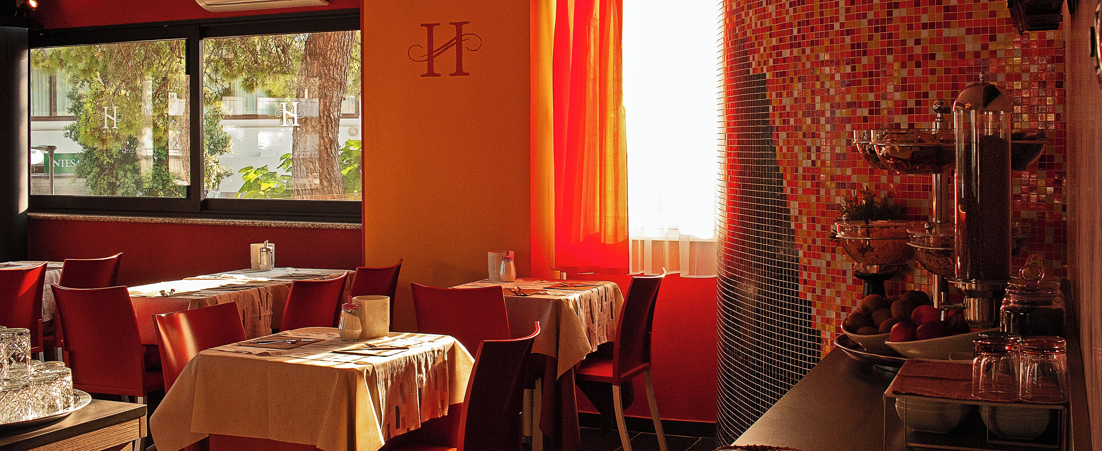 A restaurant interior with tables set for dining, a view through the window, and a tiled backsplash.