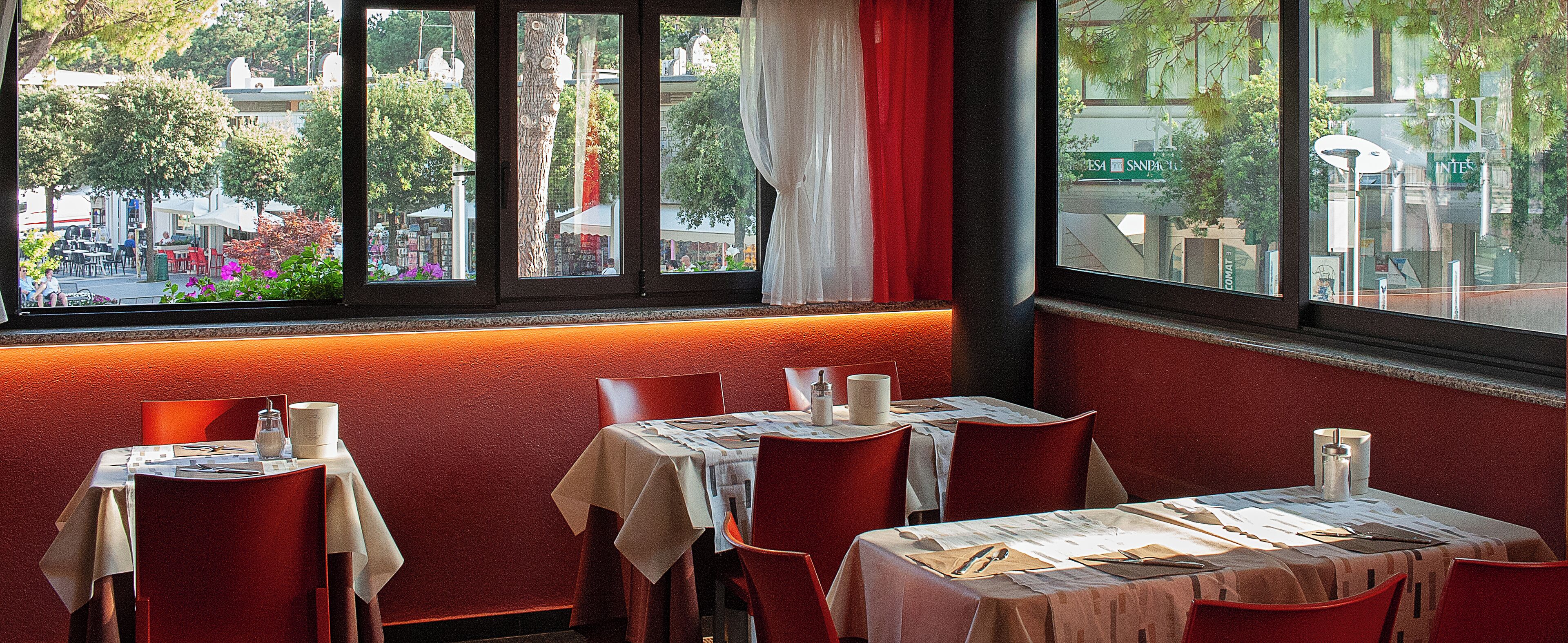Un restaurant avec des tables dressées, une vue sur la rue et un mur rouge.