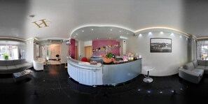 Un moderno vestíbulo de hotel con un mostrador de recepción curvo, una zona de bar y diferentes disposiciones de asientos.