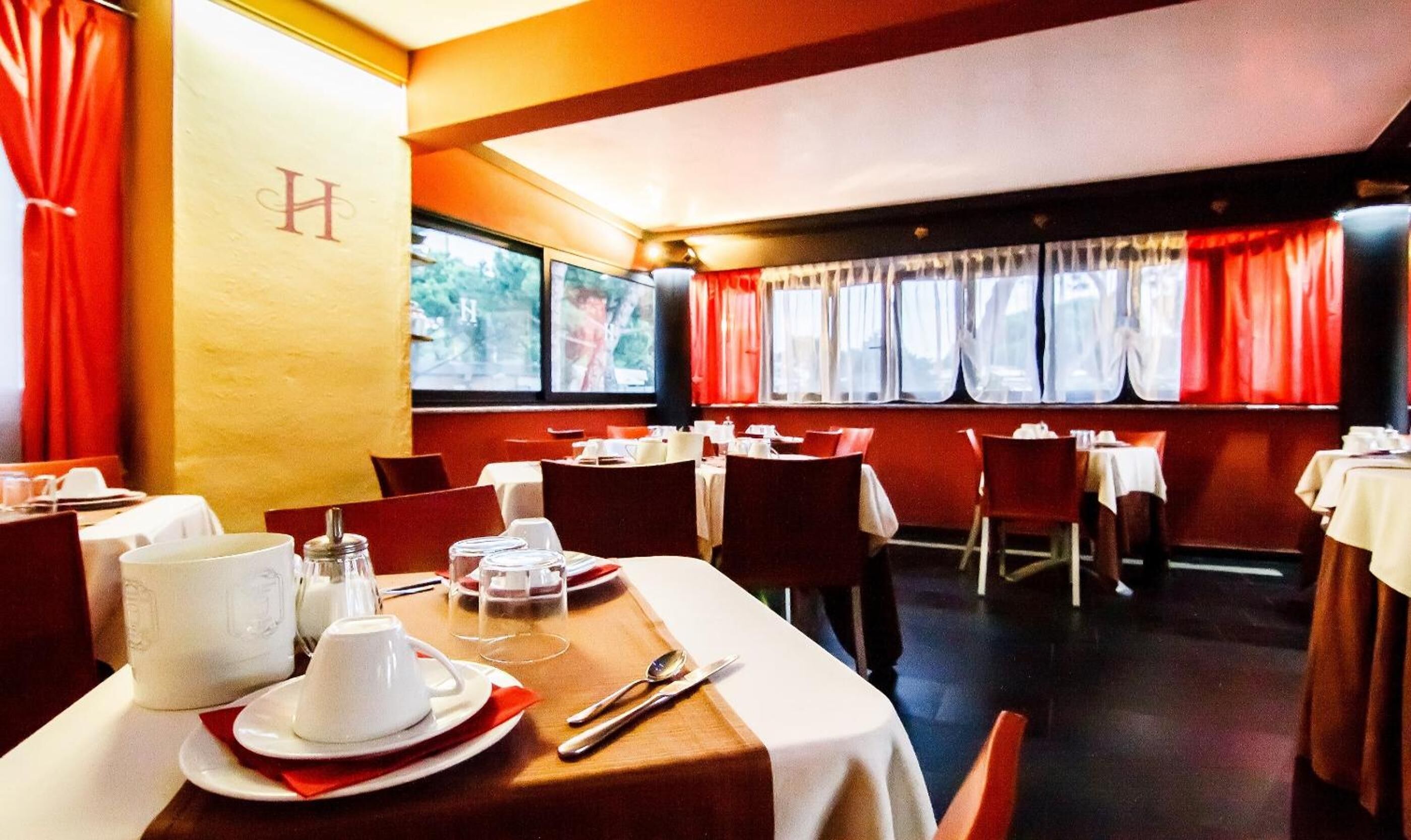 Ein Restaurantinneres mit gedeckten Tischen, roten Vorhängen und Blick durch die Fenster.