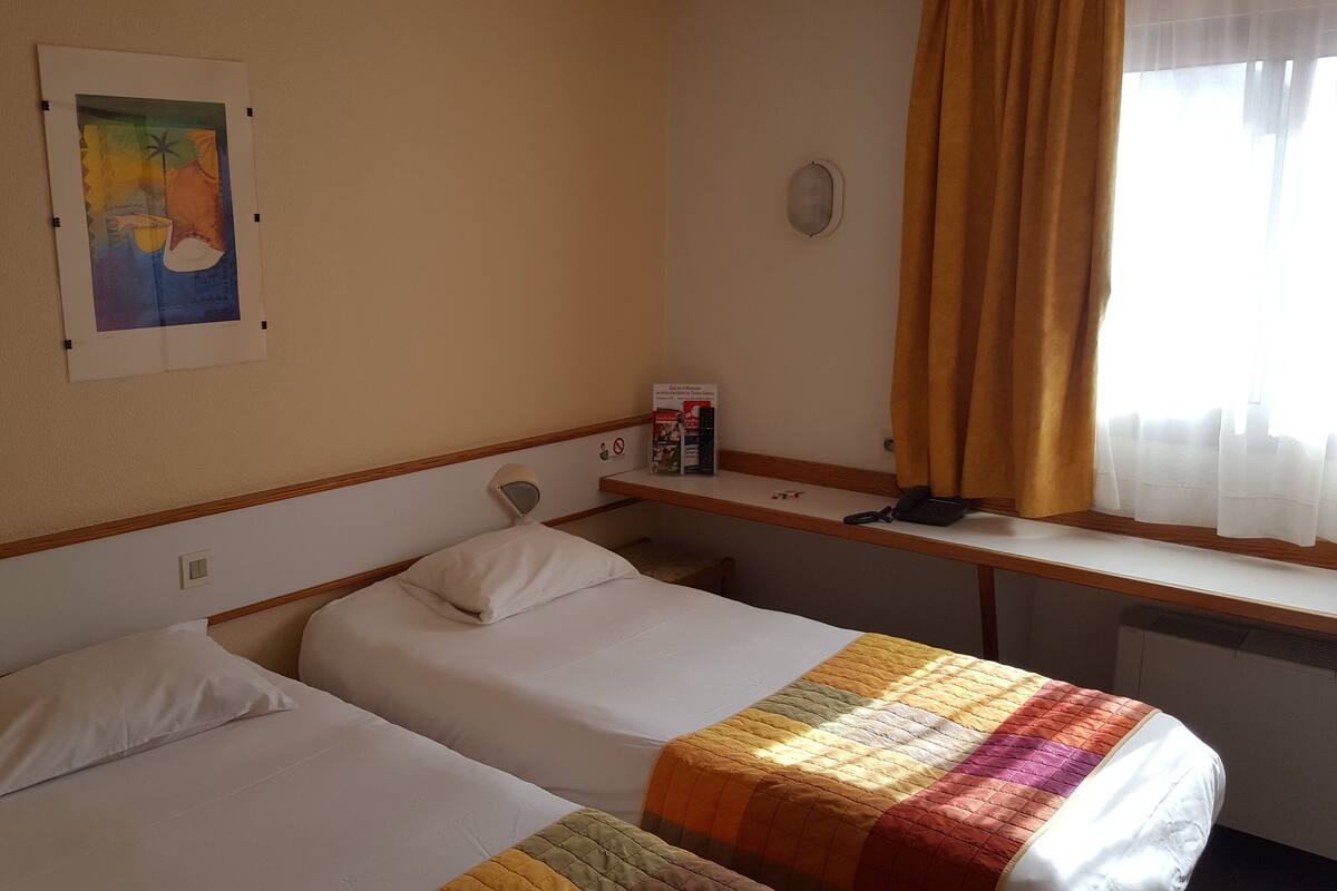 A hotel room with two beds, a painting on the wall, a desk with a phone, and a window with curtains.