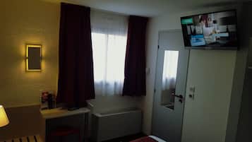 A hotel room with a bed, a desk with a lamp, a TV mounted on the wall, and a door with a mirror.