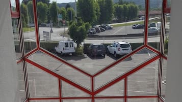 Uitzicht vanuit een raam met een geometrisch kader, op een parkeerplaats met meerdere auto's en een straat op de achtergrond.