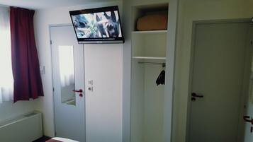 A hotel room with a television mounted on a wall, a door with a red handle, and a window with a red curtain.