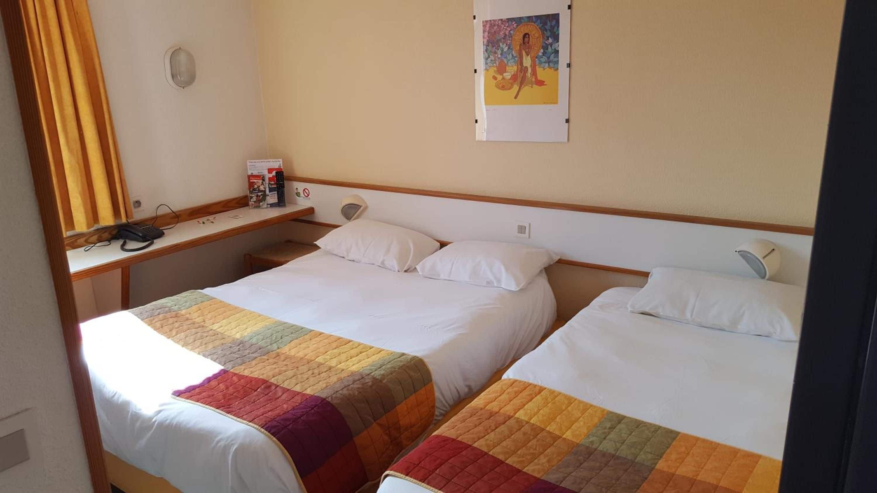 Une chambre d’hôtel avec deux lits, un bureau avec un téléphone et un tableau au mur.