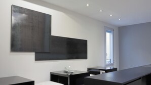 A modern, minimalist room with a large black desk, a bench, and a large abstract painting on the wall. - Muà Boutique Bologna (Bologna)