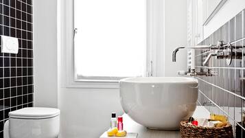 A bathroom with a large white basin, a toilet, and a window.