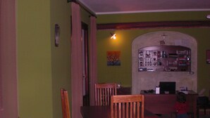 A dining area with wooden chairs and a table, a small child standing near the table, and a bar area with shelves in the background. - A Giummara (Marsala)