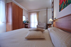 Habitación de hotel con una cama grande, un escritorio con computadora, una silla y un cuadro en la pared.