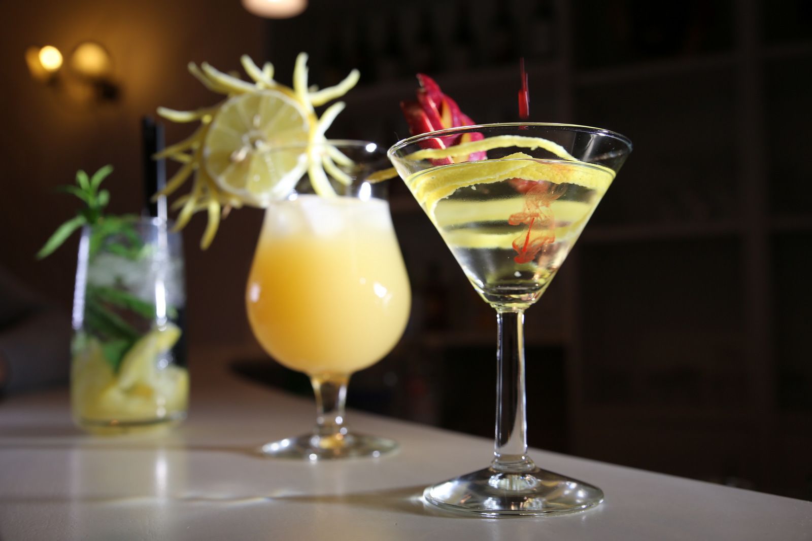 Tre cocktail su un bancone del bar, con sfondo sfocato.