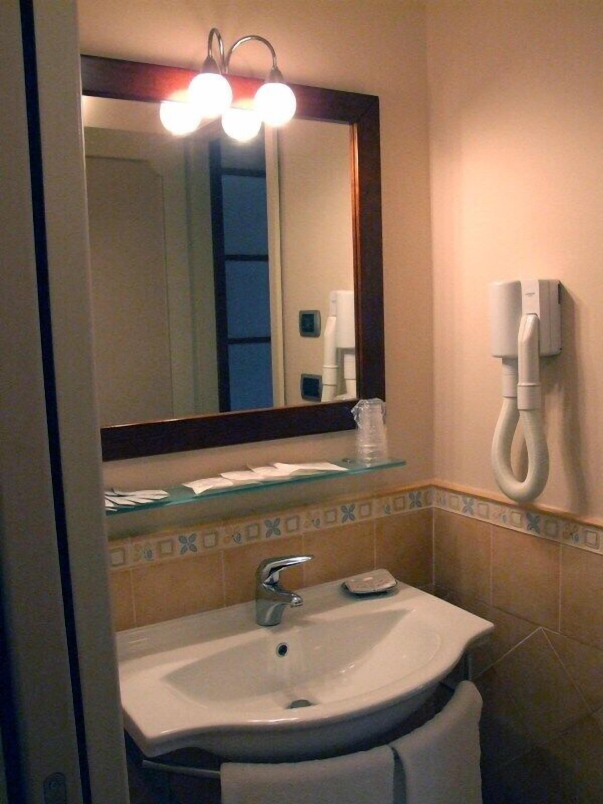 Un baño con lavamanos, espejo y teléfono fijo en la pared.