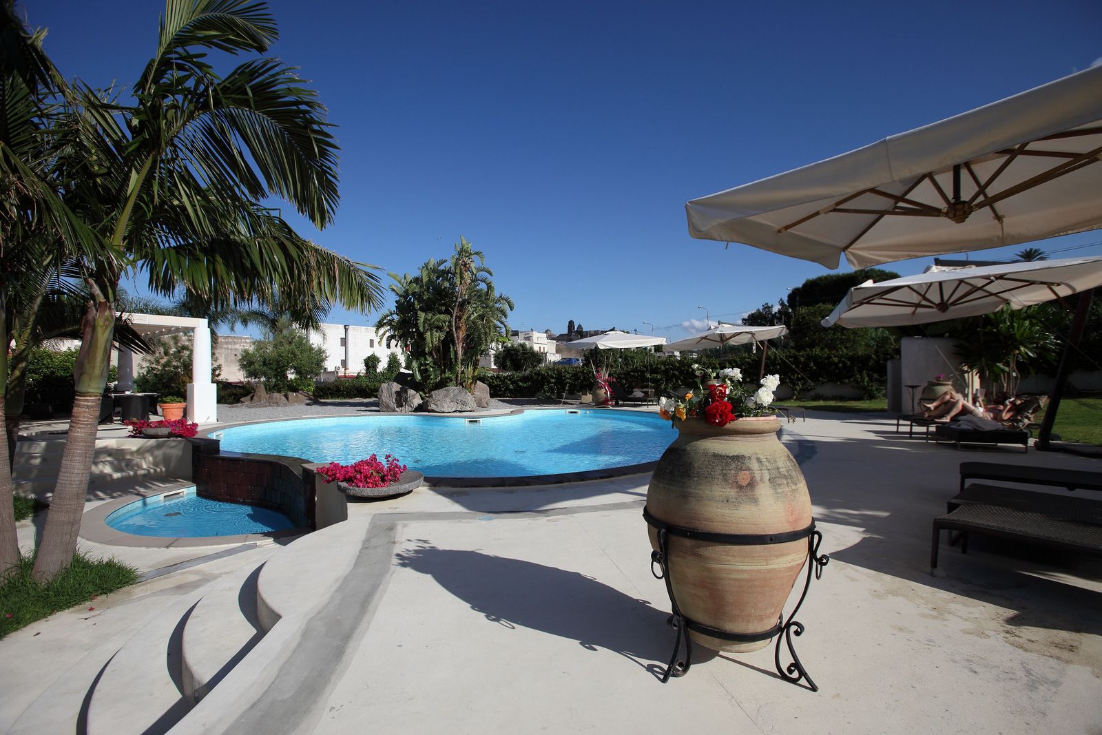 A pool area with a large central pool, smaller pools, palm trees, and outdoor seating.