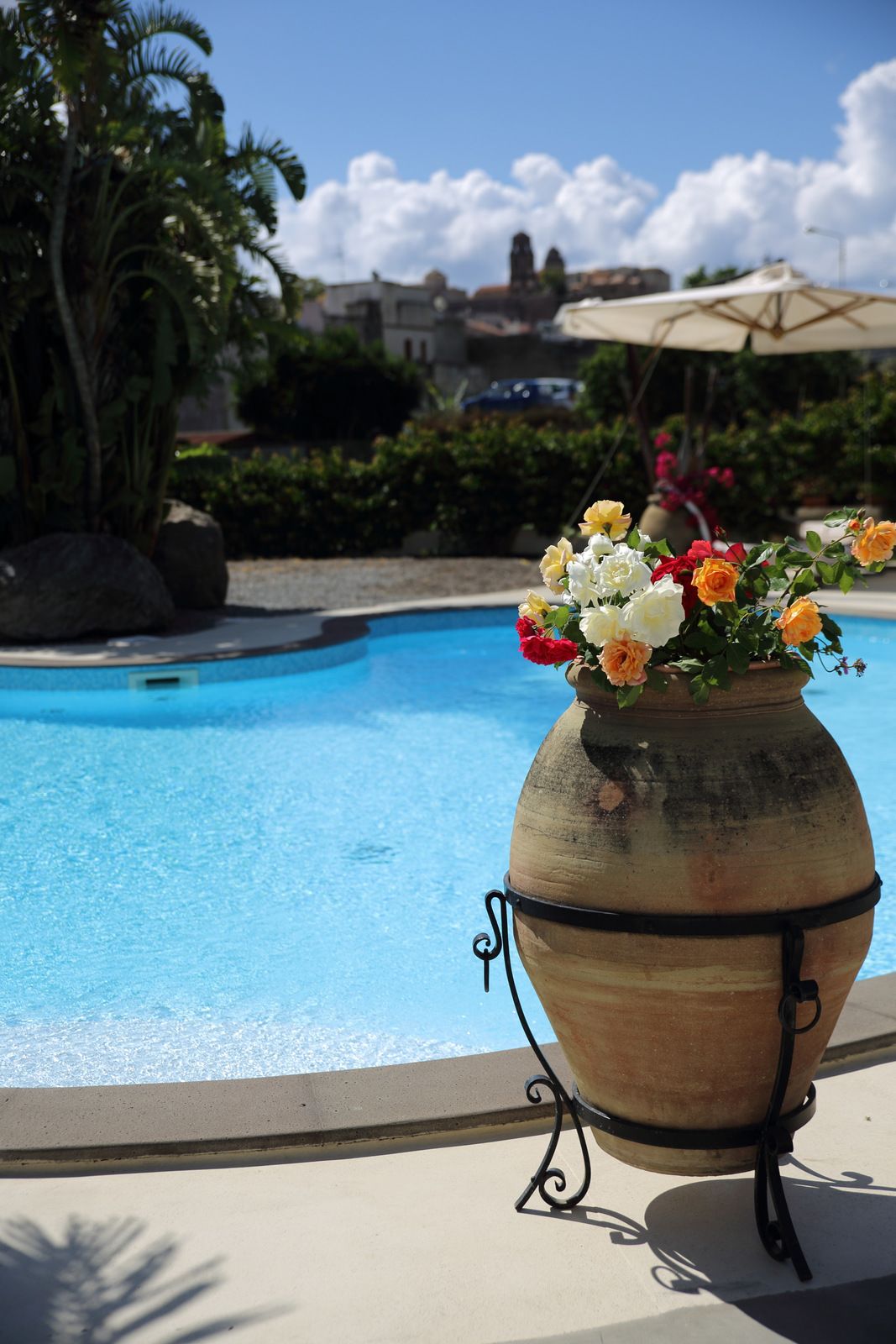 A large terracotta pot with a floral arrangement by a poolside.