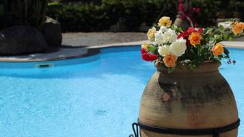 A large terracotta pot with a floral arrangement by a poolside.