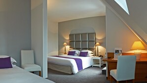 A hotel room with two beds, a desk, a chair, and a small table.