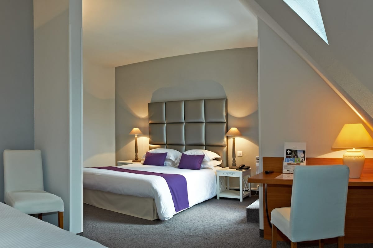 A hotel room with two beds, a desk, a chair, and a small table.
