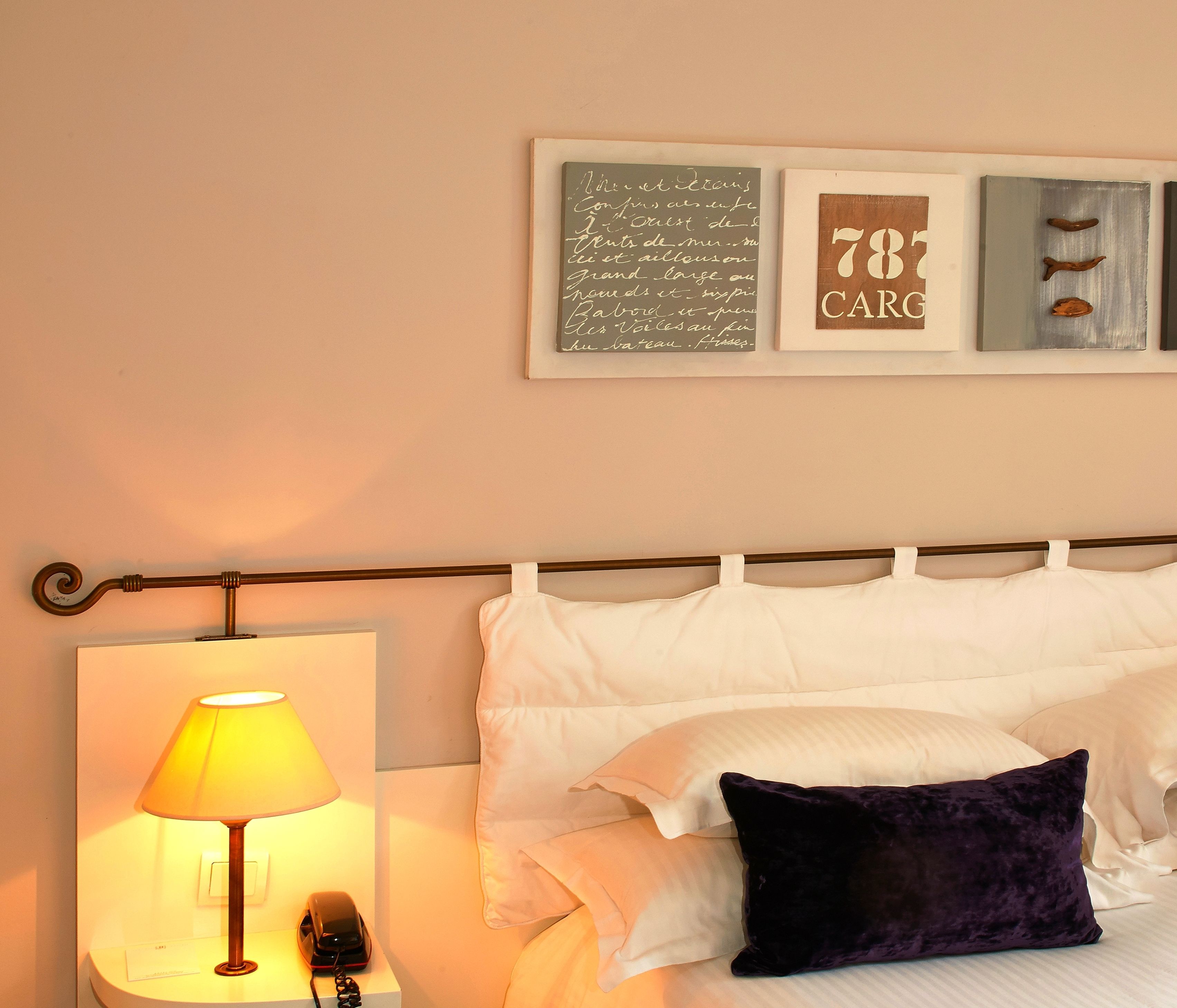 A neatly made bed with white and dark purple pillows, a bedside lamp, and a framed artwork above the bed.