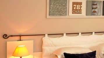 A neatly made bed with white and dark purple pillows, a bedside lamp, and a framed artwork above the bed.