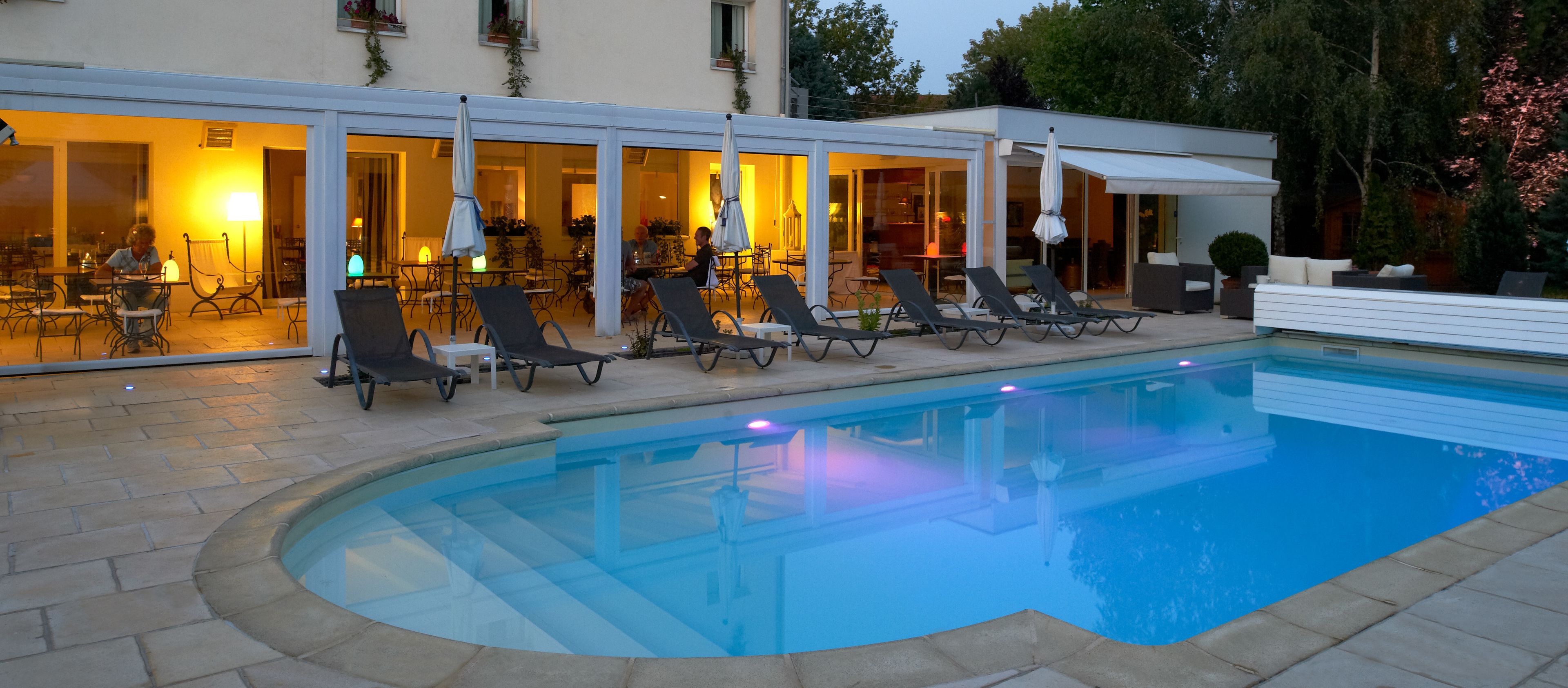 Zona de piscina con sillones de descanso y un comedor visible a través de puertas de cristal.