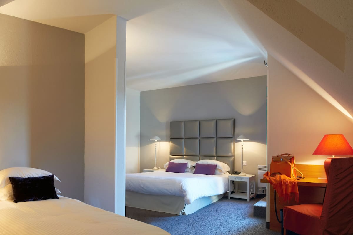 A hotel room with two beds, a desk, a chair, and a red lamp.