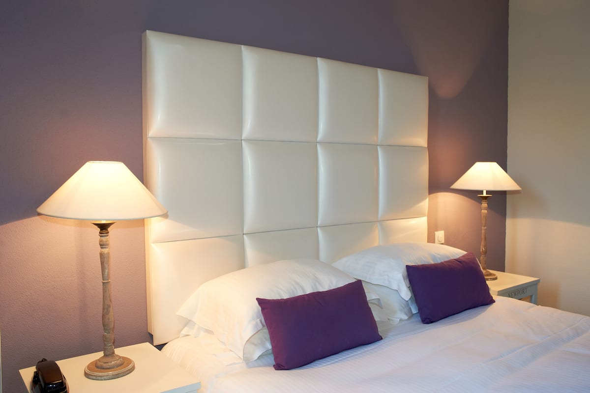 A neatly made bed with a tufted headboard, two bedside lamps, and a purple pillow.