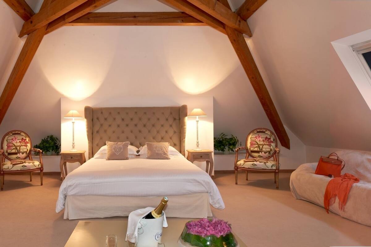 A bedroom with a vaulted ceiling, a large bed, two bedside tables with lamps, a TV, and a wooden dresser.