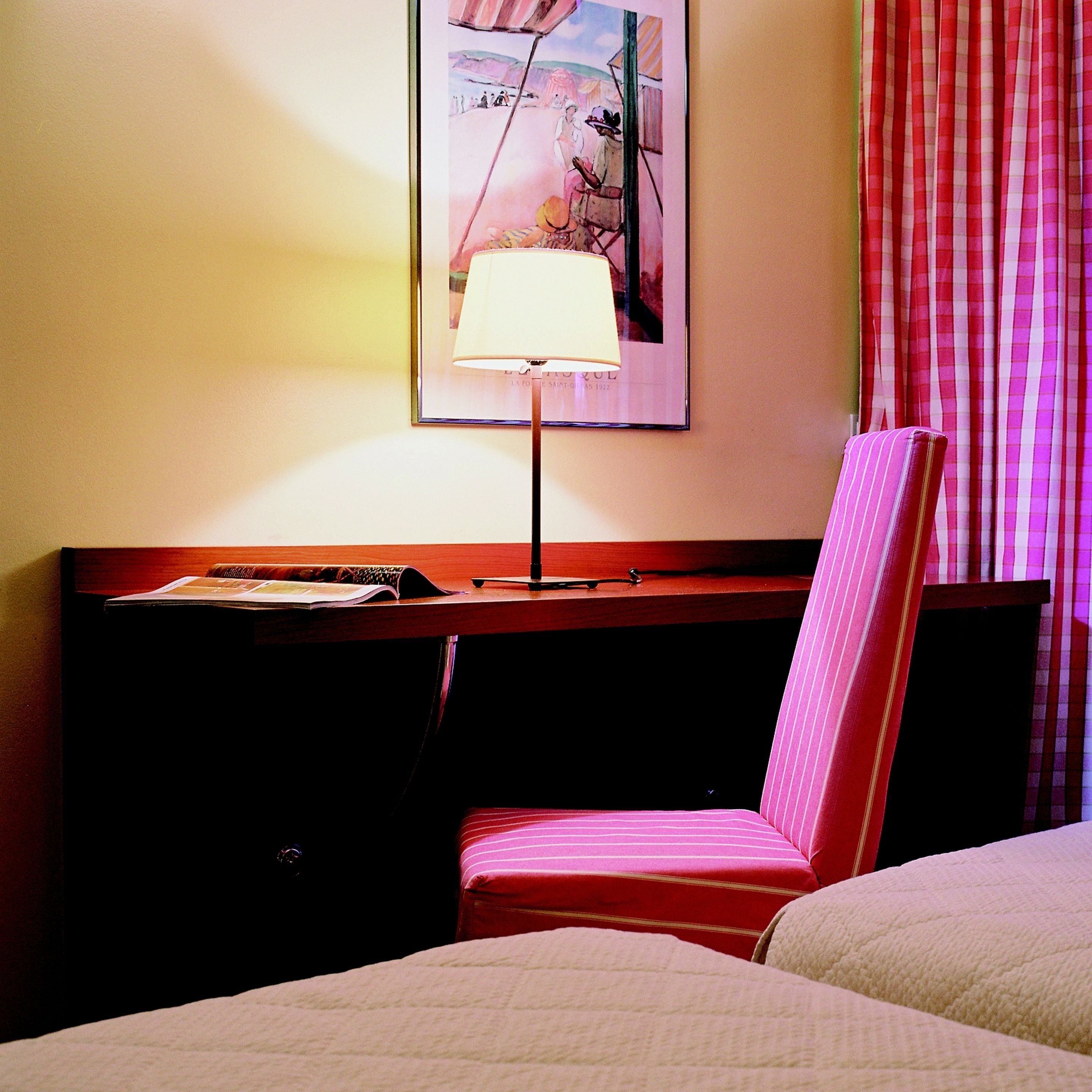 A hotel room with a bed, a desk with a lamp, and a striped chair.