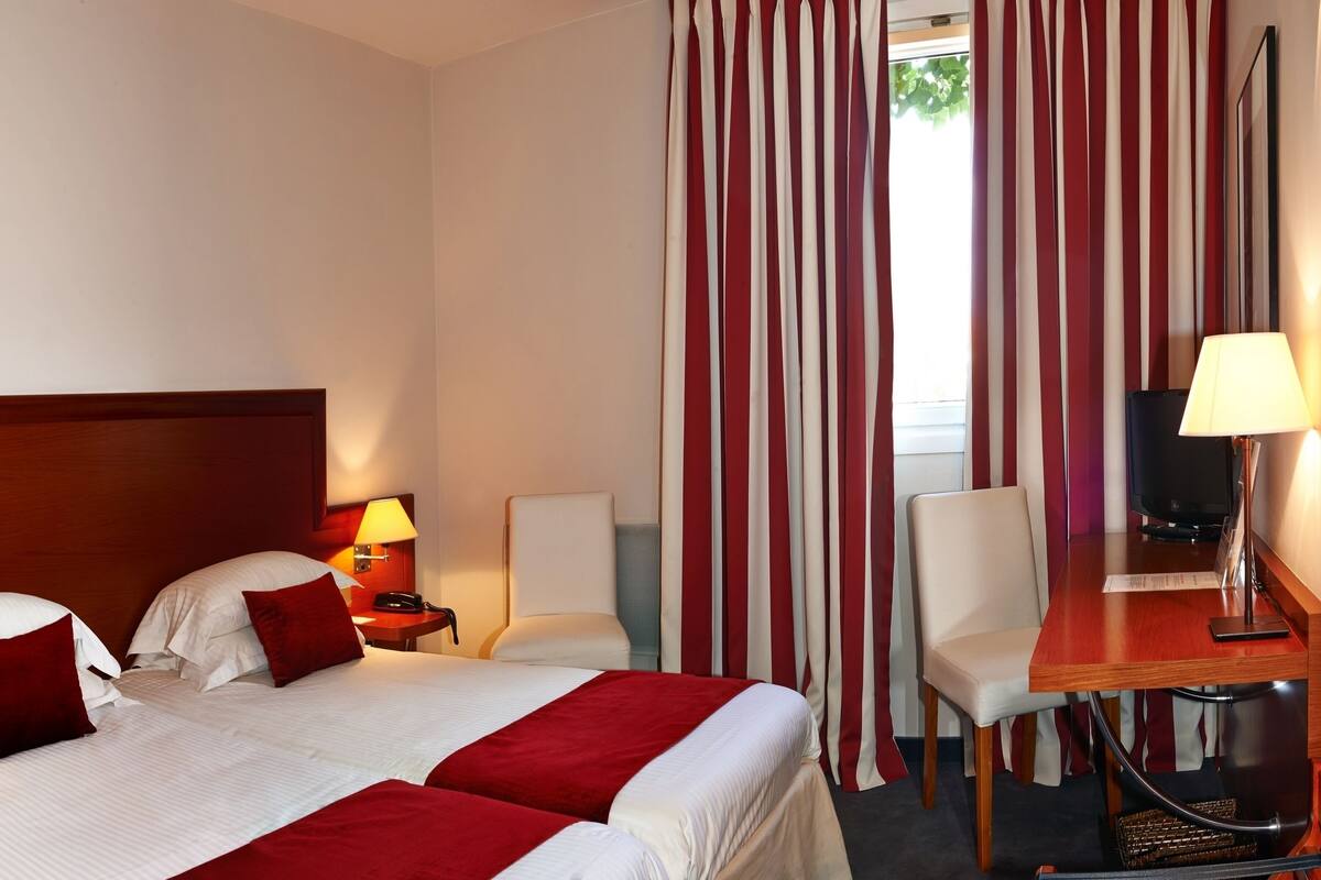 A hotel room with a large bed, two bedside tables with lamps, a desk with a chair, and a TV.