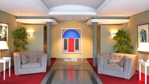 A lobby with two sofas facing each other, a red and blue door, and two potted plants.