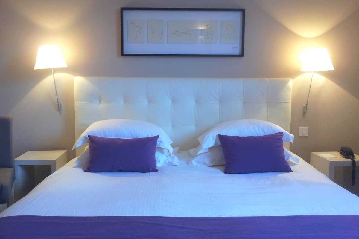 A hotel room with a large bed, two bedside lamps, and a framed artwork on the wall.