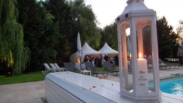 Un área junto a la piscina con sillones, un farol blanco y una zona cubierta al fondo.