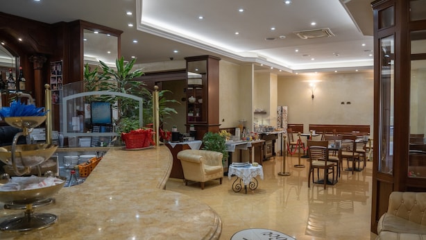 A hotel lobby with a marble reception desk, seating area, and a dining section.