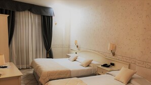 A hotel room with two beds, a desk, a chair, a nightstand with a phone, and a window with curtains.