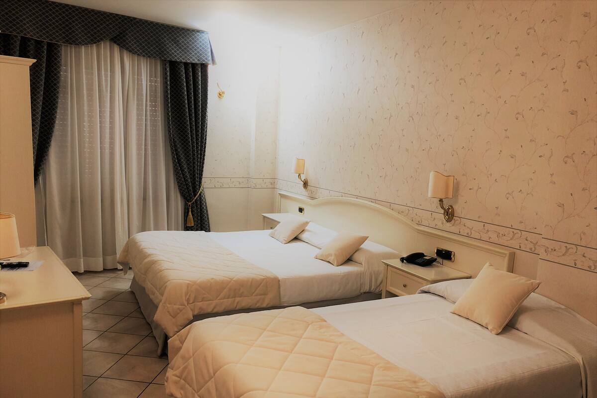A hotel room with two beds, a desk, a chair, a nightstand with a phone, and a window with curtains.