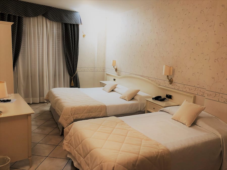 A hotel room with two beds, a desk, a chair, a nightstand with a phone, and a window with curtains.