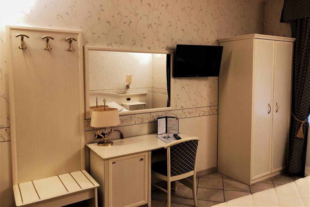 A small, compact bedroom with a single bed, a bedside table with a lamp, a wardrobe, a mirror, and a television mounted on the wall.