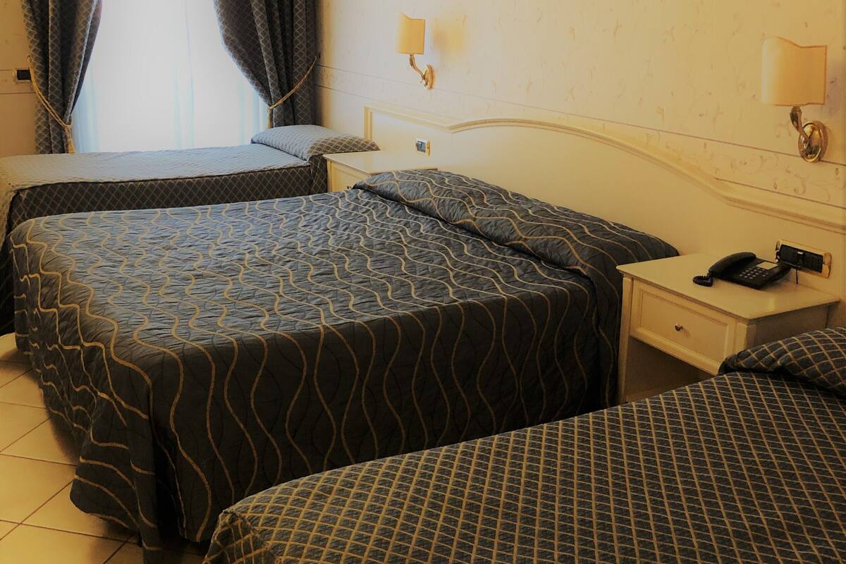 A hotel room with two beds, a nightstand with a phone, and a window with curtains.