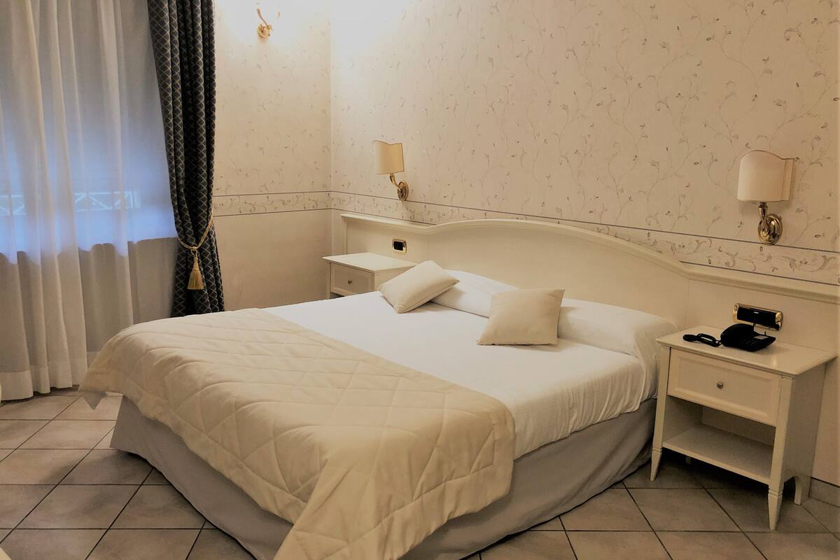 A hotel room with a large bed, two bedside tables, a nightstand, and a wall-mounted lamp.