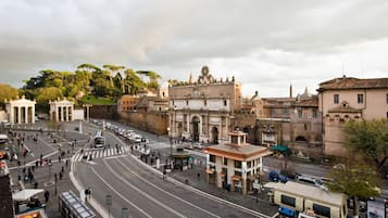 A busy urban street with historic buildings, a prominent archway, and a green park area.