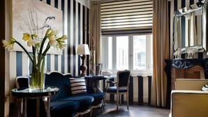 A room with striped walls, a blue sofa, a table with a lamp, and a vase with flowers. - Casa Montani (Rome)