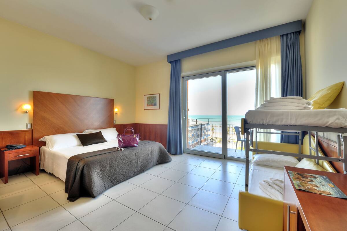 Ein Hotelzimmer mit einem Einzelbett, einem Etagenbett, einem Schreibtisch und Blick auf die Stadt.
