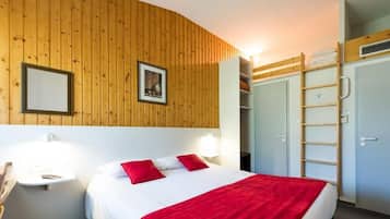 A hotel room with a wooden wall, a bed with red bedding, a bedside table with a lamp, a wardrobe, and a ladder.